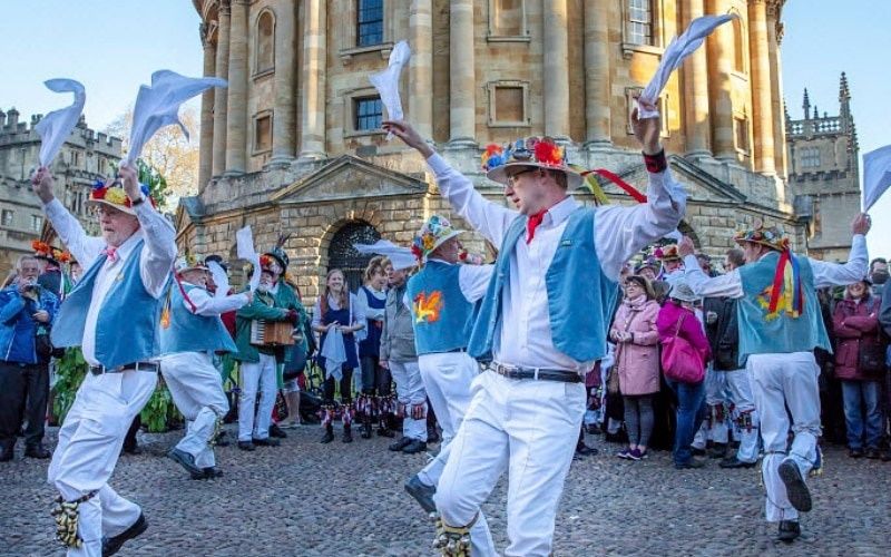 Morris dancers wave white handkerchiefs outside a historic Oxford building